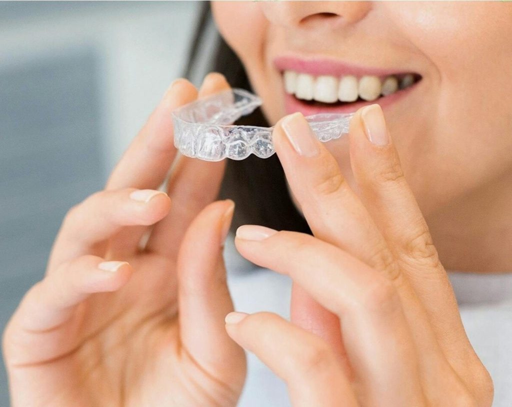 Close-up of a woman holding an Invisalign dental aligner, showcasing dental health and a bright smile.